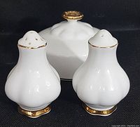 Front view of two salt and pepper shakers with butter dish lid behind, showing white bone china with gold trim and floral gold knob on lid.