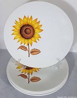 Photo of four white ironstone plates with a bright sunflower design stacked and one plate upright on a display stand.
