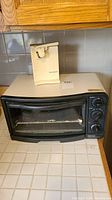 Betty Crocker compact toaster oven with Kitchen Works electric can opener on top, sitting on a tiled kitchen counter.