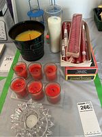 Photo showing citronella candle, seven red votive candles in glass, two blue metal and glass holders, tall white pillar candle, boxed red taper candles, and clear glass decorative candle holder.