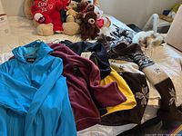 Seven coats, hoodies, and housecoat spread on a bed, showing various colors and styles including blue, burgundy, yellow, white with fur hood, and knitted brown patterned.