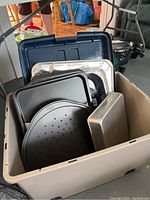 Plastic bin filled with various baking sheets, pans, and toaster partly visible in plastic wrap.