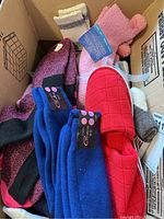 View of assorted socks in box including blue, pink, red, beige and grey in different styles and textures with sock hangers