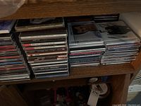 Stacked CDs on wooden shelves, showing variety of album covers and titles including Andrea Bocelli.