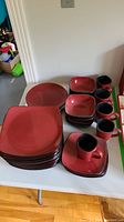 Full set of red square stoneware dishes including various plates, bowls, and mugs displayed on a table.