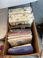 Box showing stacked packages of curtains and sheets, floral printed curtains visible and assorted bags identifiable.