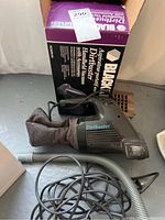 Black & Decker Dirtbuster vacuum cleaner shown with original box in background, fabric filter bag attached, power cord and hose laid out in foreground.
