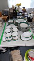 Set of Royal Heritage porcelain dishes including stacked plates, cups, and serving pieces on a table with a busy room background.