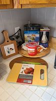 Overview of kitchenware items on counter including wooden Lazy Susan, cutting boards, food chopper, and metal grater.