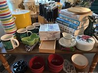 Photo showing various kitchenware items including mugs, canisters, porcelain cup and box, and a stack of books.