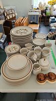 Full set of Mountain Wood stoneware dishes displayed on white table showing plates, bowls, mugs, creamers, sugar bowl, and salt and pepper shakers.
