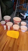 Overview of all items including large and medium popcorn bowls, small snack bowls, two salt and pepper shakers, and yellow plastic butter dish on a wooden floor.