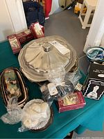 Table with silver plated serving trays and dish, napkin rings, and boxed items including coasters and wedding bell.