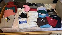 Wide view of assorted men's undershirts, socks, golf shirts, ladies' shirts, winter sweaters, and pajamas arranged on mattress