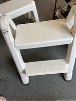 White plastic folding step stool from side angle showing two steps with textured surfaces.