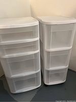Two white plastic storage bins side by side against a wall on a painted floor, showing overall size and drawer count