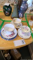 Three tea cup sets and four saucers displayed on a wooden table with other decorative items nearby.