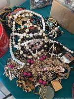 Tin container filled with mixed costume necklaces showing white, black, pink beads, and gold-tone chains