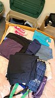Folded assorted women's clothing including hoodies, pants, and shirts in multiple colors laid out on mattress