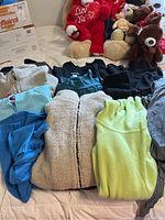 Overview of multiple women's fleece and knit clothing items in size large, various colors and textures laid out on bed.