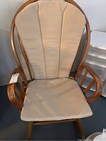 Front view of wooden rocking chair with beige cushion on seat and backrest.
