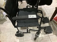 Side and top view of the black Airgo ultra-light folding wheelchair showing padded armrests, seat, small wheels, and detachable footrests.