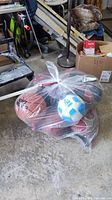 Lot of sports balls including basketballs in a plastic bag on floor among other items