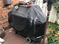 Covered Weber barbecue on patio with wheels visible