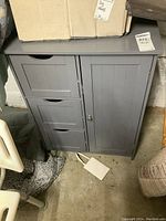 Front view of painted MDF cabinet showing one door on the right and three horizontal drawers on the left, in a grey finish.