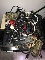 Top view of assortment of tangled cables in various colors and connector types including red, black, white, and clear cables, with some connectors visible.