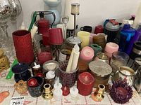 Wide view of assorted candles and holders on table, showing various colors and styles of candles and glass and metal candle holders.