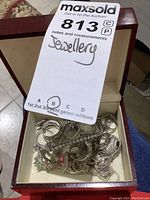 Photo of a beige-lined wooden jewellery box holding multiple rings and a rhinestone bracelet with a MaxSold auction tag visible.