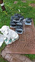 Stack of seven black solar powered deck lights on a brown welcome mat showing weathered condition.