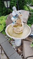 Front view of the resin outdoor fountain with two children figurines showing weathering and moss buildup in the basin.