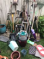 Wide view showing full lot against a wooden fence outdoors, tools arranged upright and several flower pots in front.