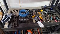 Shelf displaying various hand tools including wrenches, pliers, metal square, and other small tools.