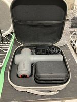 Full massager kit in open carrying case showing massager, charger, and smaller case