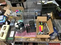 Overview of office supplies including wire mesh organizers, calculators, pens, and sticky notes spread on a table.