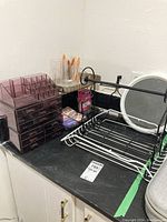 Photo showing purple acrylic makeup organizer with drawers, clear brush holder, black metal rack, round white framed mirror and some facial supplies