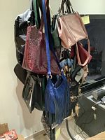 Assortment of approximately twenty purses and bags hanging from hooks, showing variety of colors and styles including leather and fabric.