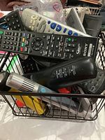 Wire basket filled with assorted remote controls showing various brands and designs including Sony and Panasonic.