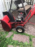 Side view of red MTD snow blower with black snow chute and tires, showing general wear and dirt.
