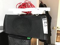 Front view of KEF black center speaker with mesh grill, white mounting bracket on top, and red speaker wire bundled on top.