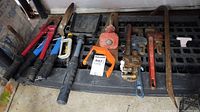 Full view of all tools arranged on a grated surface including three pipe wrenches of various sizes, bolt cutters, pruning shears, clamp, saw, and a crowbar.