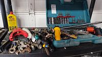 Full view of workbench showing assorted tools including clamps, wrenches, electric screwdriver, and socket sets in case.