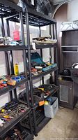 Black plastic shelving unit filled with tools and other items to show scale and structure, with garage background.
