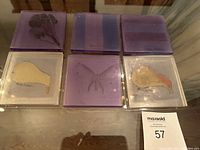 Photo of six handmade acrylic drink coasters arranged in two rows of three. Visible batik silk inlays include flowers, butterfly, fruit, and patterned stripes. Coasters show some wear and use.