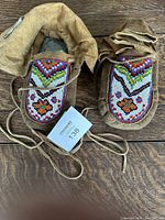 Top view showing pair of brown leather moccasins with colorful beadwork on the uppers and leather ankle ties.