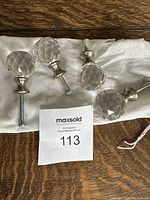 Set of four faceted crystal drawer pulls displayed on a white cloth atop wooden surface, showing silver-colored metal bases and attached threaded rods.