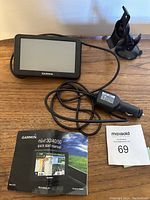 Garmin GPS unit with screen and attached charging cable, quick start manual and auction lot card on table.